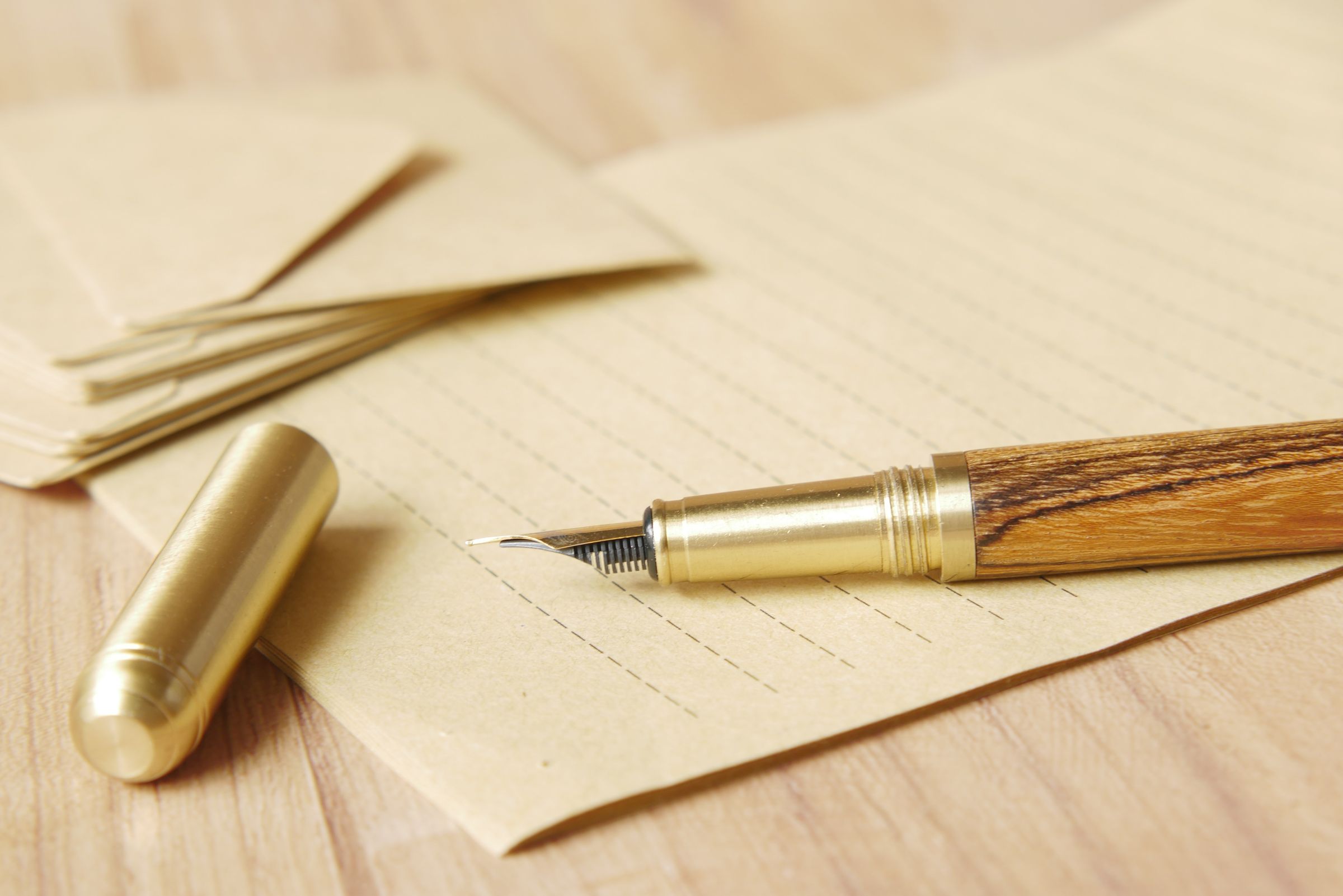 A brass fountain pen uncapped on kraft lined paper.