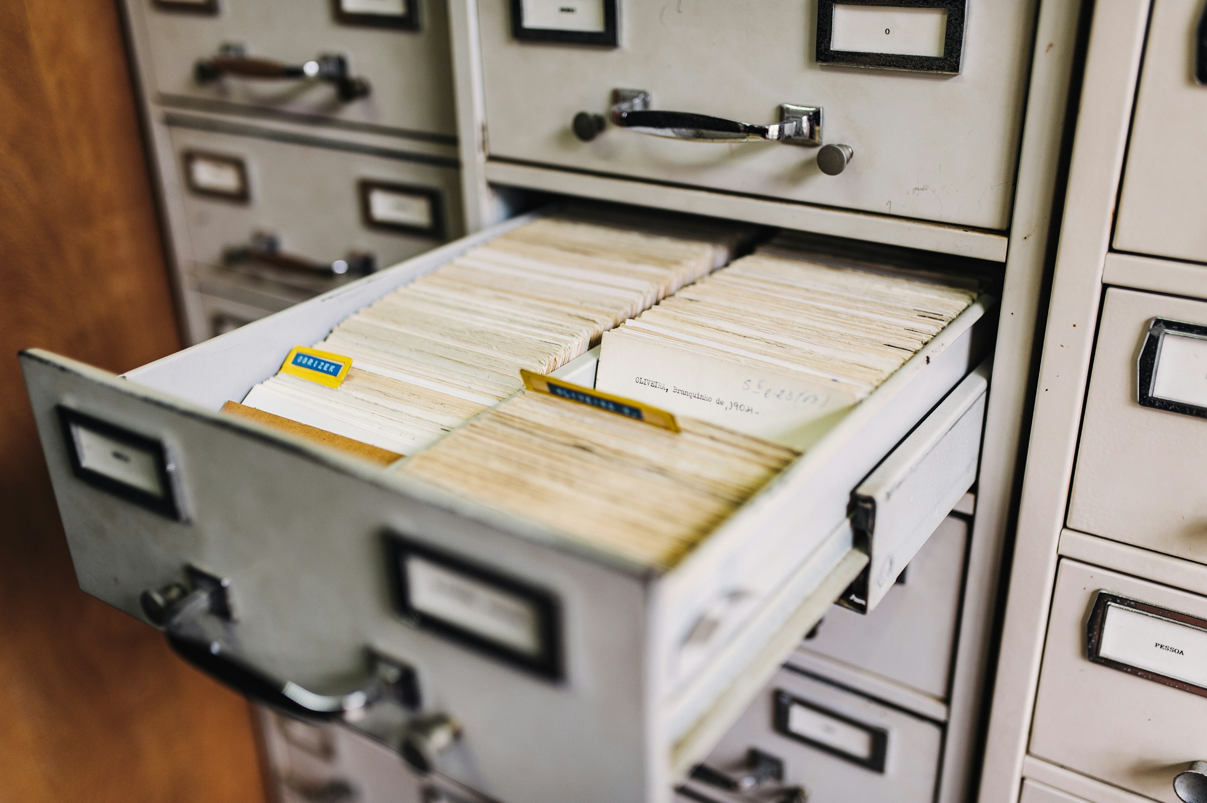 An open drawer of a metal card catalog, index cards packed in rows, other drawers closed around it.