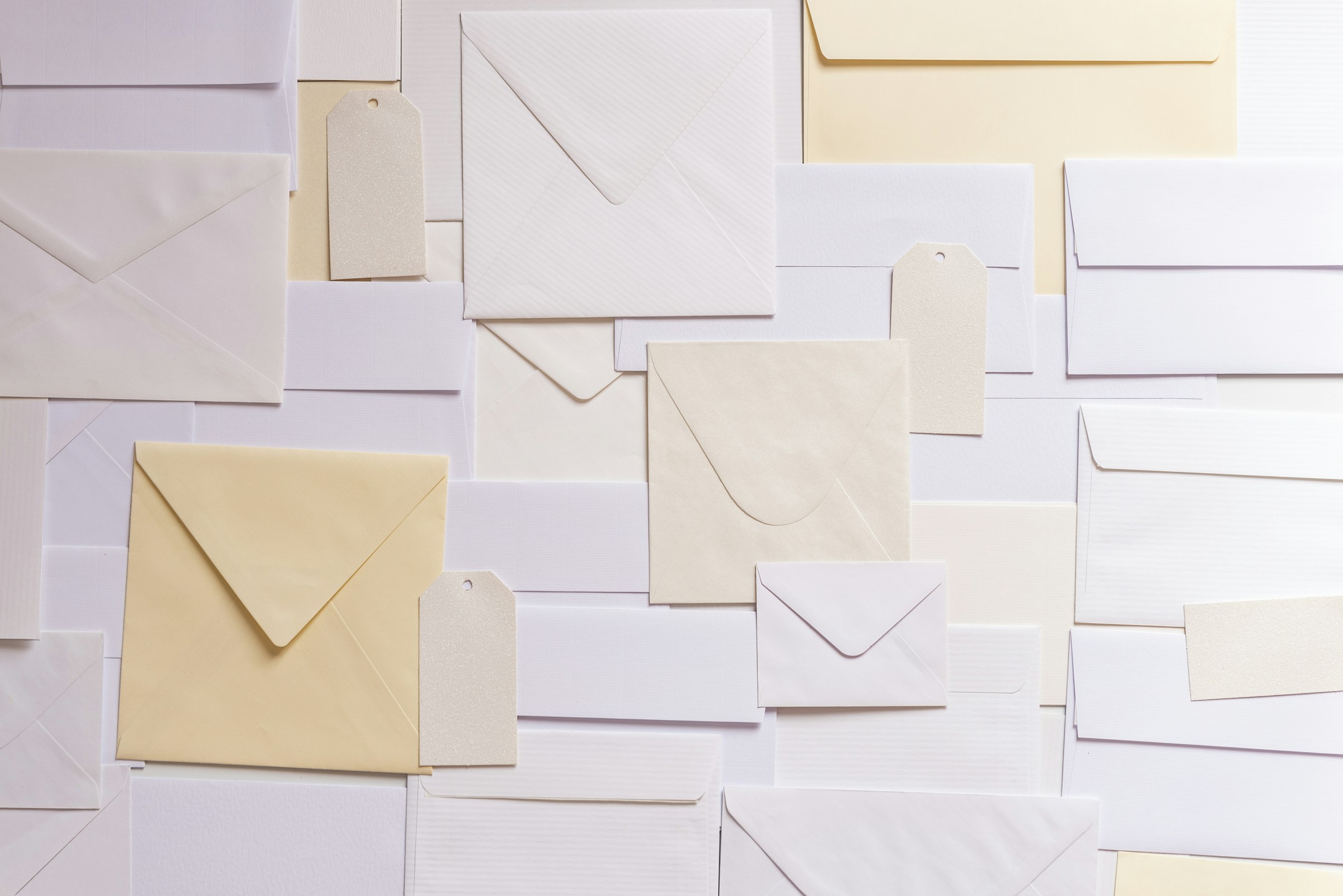 Cream and white envelopes and paper tags laid flat and overlapping on a pale surface.