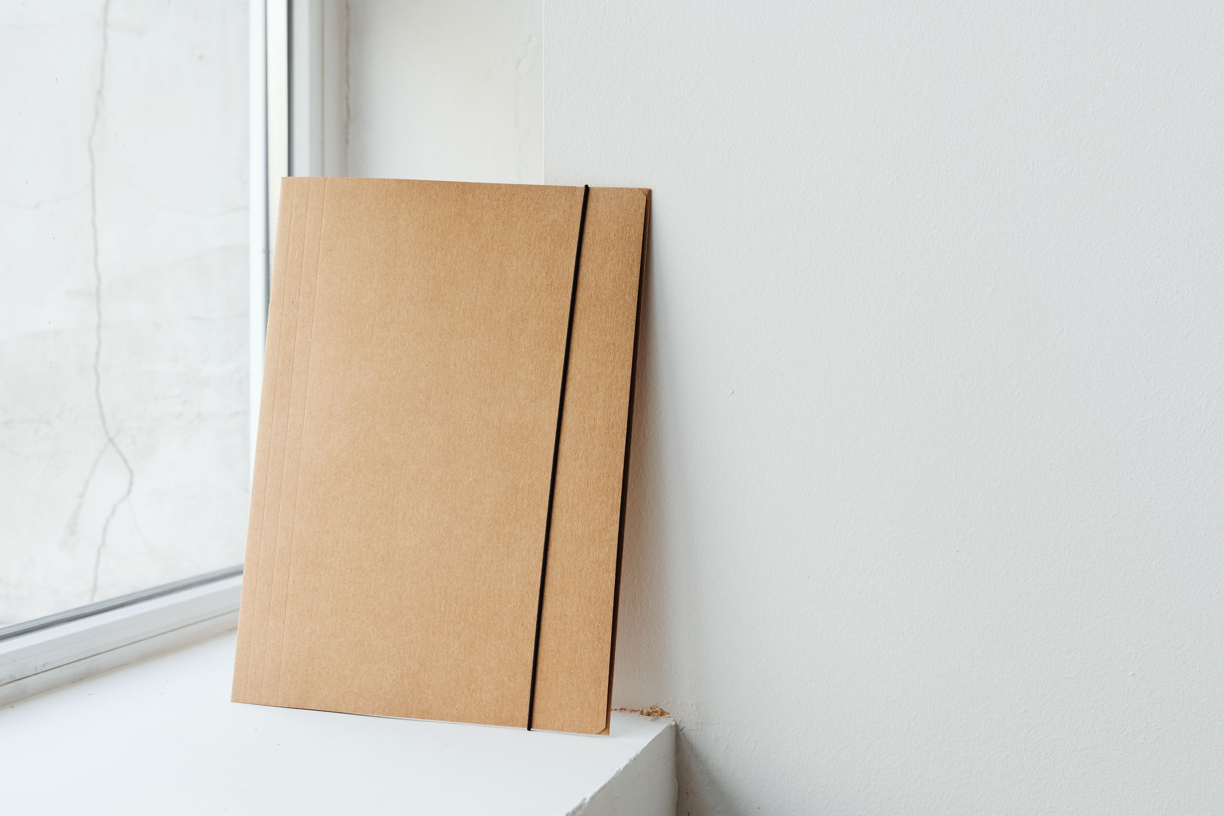 A single kraft folder with an elastic band standing on a white windowsill.