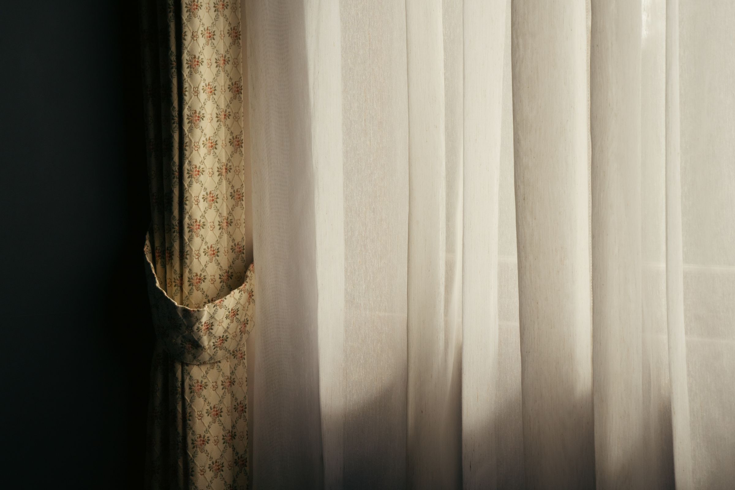 A sheer white curtain in front of a window, light coming through the folds.