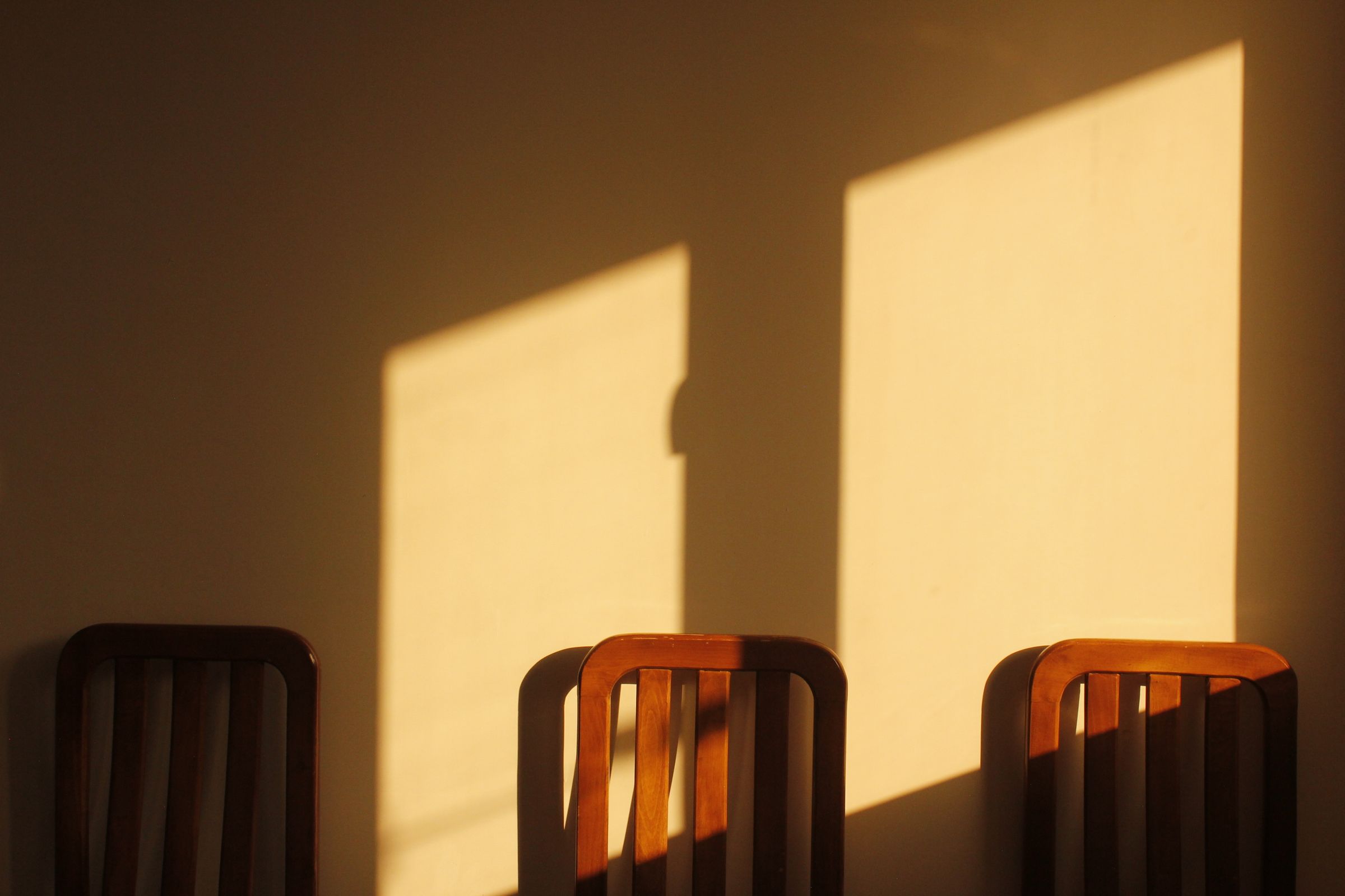Three wooden chair backs against a wall lit by two windows in late afternoon.